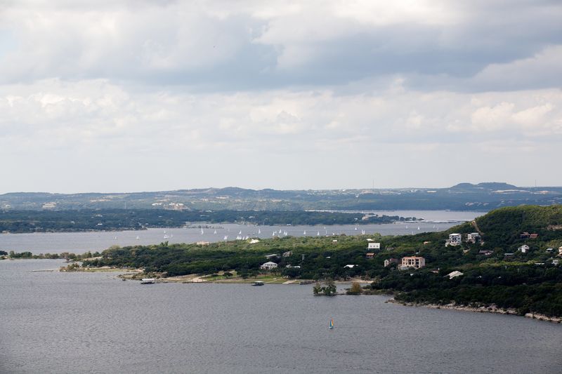 Lake Travis at full capacity, with green Hill Country hills along the shoreline under a cloudy sky