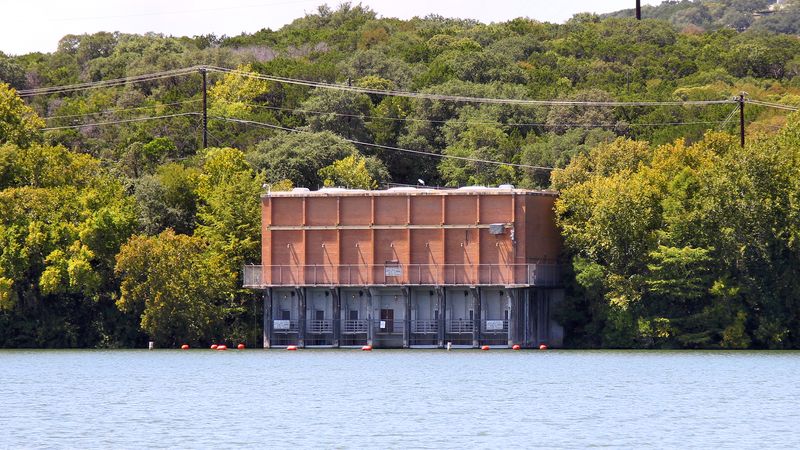Brick water intake building of Austin's Ullrich Water Treatment Plant on the shore of Lake Austin, backed by wooded hills